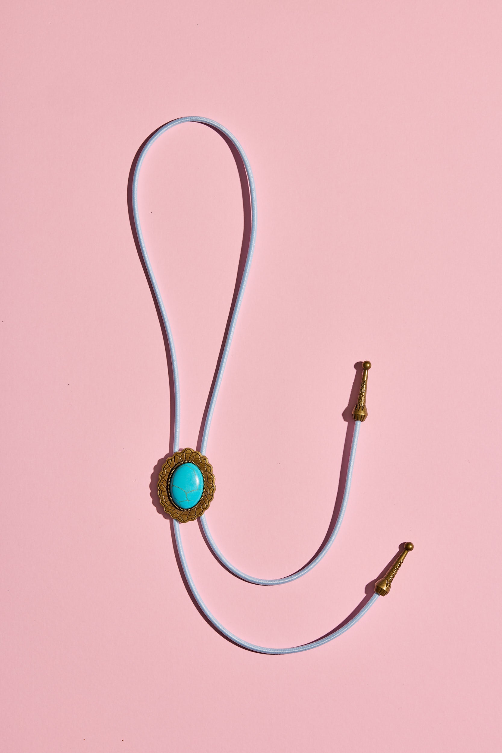 Handmade bolo tie with bright coloured cord and brass turquoise-look hardware, displayed on neutral background – western costume jewellery made in Australia