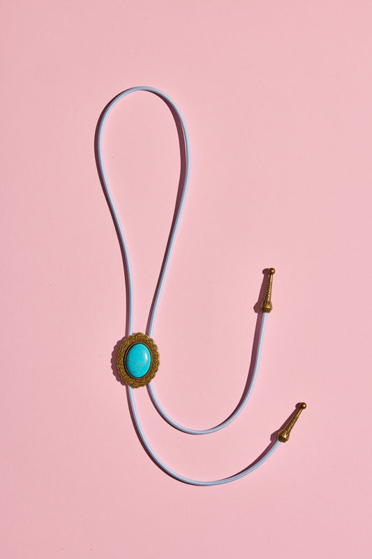 Handmade bolo tie with bright coloured cord and brass turquoise-look hardware, displayed on neutral background – western costume jewellery made in Australia